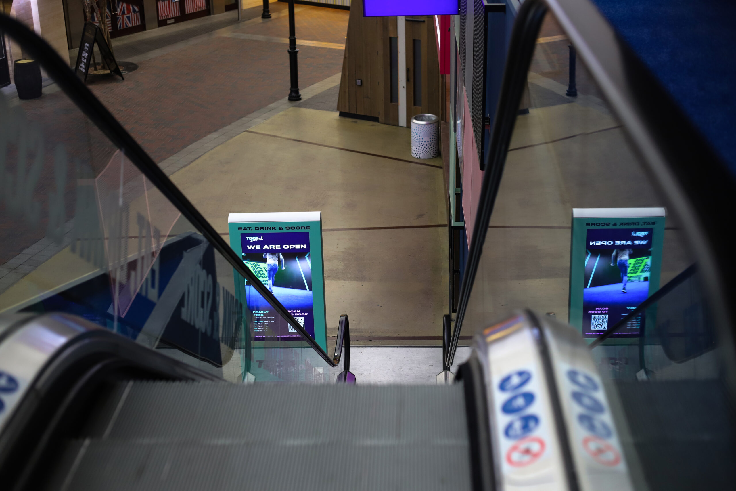 View from escalator of Digital totem at TOCA Social, displaying promotions